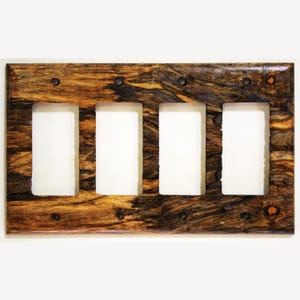 Puede incluir: Una placa de cubierta de interruptor de luz de cuatro módulos de madera con un patrón de vetas de madera natural. La cubierta tiene cuatro aberturas rectangulares para los interruptores y está asegurada con tornillos de color oscuro. La madera tiene tonos marrones y negros.