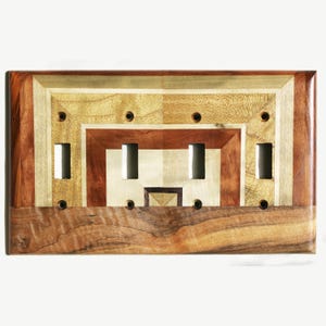 Könnte beinhalten: Ein Holz-Lichtschalter-Abdeckung mit einem geometrischen Design, das mehrere Holztöne aufweist, darunter Braun, Beige und helles Holz. Die Abdeckung hat vier Schalteröffnungen.