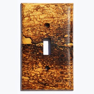 May include: A light switch cover made of wood with a unique brown and yellow burl pattern.