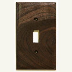 May include: A rectangular, dark brown wooden light switch cover with a glossy finish. It has a single toggle switch opening and two screw holes. The wood grain is visible, adding texture to the design.