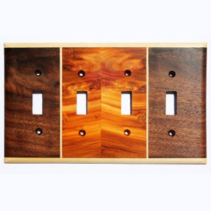 May include: A triple light switch plate made of wood with a walnut, maple, and cherry wood veneer. The switch plate has a light brown border.