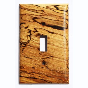 May include: A light brown wooden light switch cover with dark brown wood grain patterns.
