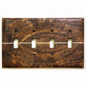 Könnte beinhalten: Eine rechteckige Lichtschalterabdeckung aus Holz mit einem dunkelbraunen, wirbelnden Maserungsmuster. Sie hat vier weiße Kippschalteröffnungen und eine dünne, horizontale weiße Linie. Die Abdeckung hat vier Schraubenlöcher zur Montage.
