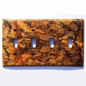 Könnte beinhalten: Eine Holz-Lichtschalterplatte mit einem natürlichen Holzmaserungsmuster in Braun-, Orange- und Schwarztönen. Die Platte hat vier Schalteröffnungen.
