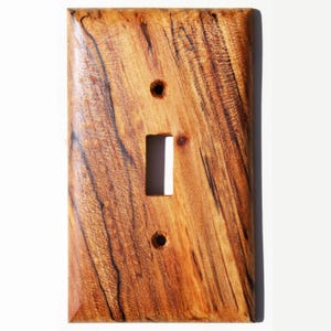 Peut inclure: Plaque de recouvrement d'interrupteur en bois rectangulaire avec une ouverture pour interrupteur à bascule et deux trous de vis. Le grain du bois est brun clair et foncé, avec un aspect naturel et texturé. Conçu pour un interrupteur standard.