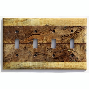 Könnte beinhalten: Eine Holz-Lichtschalterplatte mit vier Kippschalteröffnungen. Die Platte hat ein natürliches Holzmaserungsmuster mit Braun- und Beigetönen. Die rechteckige Platte hat ein rustikales Aussehen.