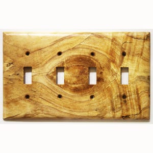 Könnte beinhalten: Eine Holz-Lichtschalterplatte mit vier Schalteröffnungen und acht Schraubenlöchern. Die Platte hat ein natürliches Holzmaserungsmuster in Beige- und Brauntönen mit glänzendem Finish. Die Platte ist rechteckig.