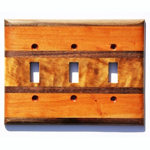 May include: A wooden light switch cover with three toggle switches. The cover is made of cherry and walnut wood with a striped pattern.