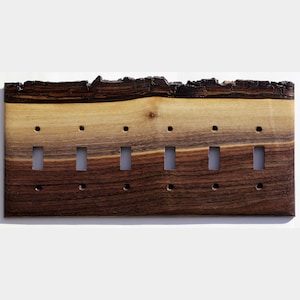 May include: A wooden light switch plate with six switch openings. The plate is made of natural wood with a dark brown and tan colour gradient. The top edge has a rough, bark-like texture.