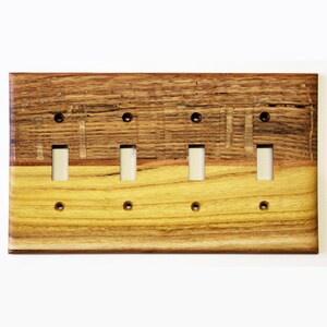 Könnte beinhalten: Ein Lichtschalterabdeckung aus Holz mit vier Kippschaltern. Die Abdeckung besteht aus zwei verschiedenen Holzarten, einer dunkelbraunen und einer hellbraunen. Das Holz hat eine natürliche Maserung.