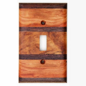 May include: Wooden light switch cover with a rectangular design. The cover features alternating bands of light and dark brown wood, with a single switch opening and two screw holes. The wood grain is visible.