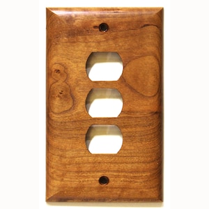 May include: A wooden triple-gang electrical socket cover plate. The plate is stained a warm brown colour, with visible wood grain. It features three oval openings for sockets and two screw holes, one at the top and one at the bottom.