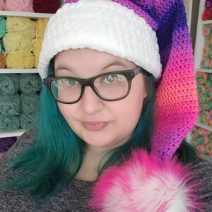 May include: A crocheted Santa hat with a white pom-pom and a gradient of pink, purple, and blue colors.