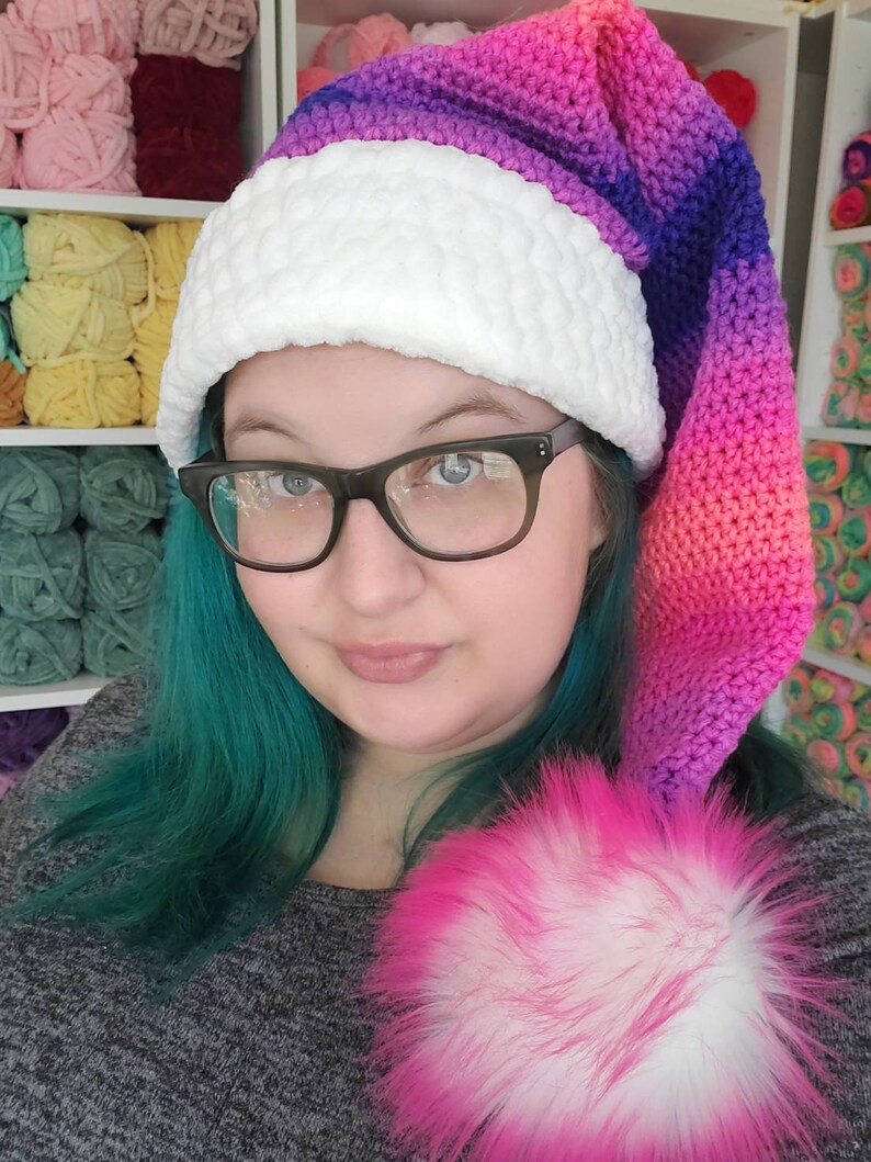 May include: A crocheted Santa hat with a white pom-pom and a gradient of pink, purple, and blue colors.