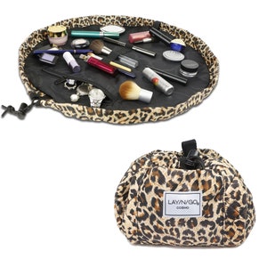 May include: A leopard print makeup bag with a drawstring closure. The bag is open and laid flat, revealing a variety of makeup and beauty products. The bag has a label that reads "LAY'N/GO COSMO".