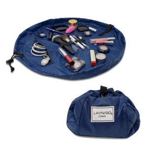 May include: A blue travel makeup bag with a quilted design. The bag is open and laid flat, revealing a variety of makeup products and accessories. The bag has a zippered pocket and a drawstring closure. The bag is labeled "LAYN/GO COSMO".