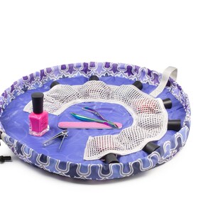 May include: A purple and white patterned round makeup bag with a drawstring closure. The bag is open and filled with various makeup and nail care items, including nail polish, nail clippers, and a nail file.