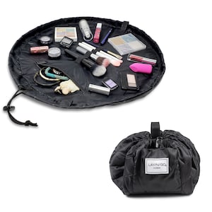 May include: Black round makeup bag with a drawstring closure. The bag is open and filled with makeup brushes, lipstick, eyeshadow palettes, and jewelry. The bag is labeled "LAYN/GO COSMO".