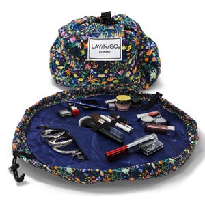 May include: A blue and floral print makeup bag with a drawstring closure. The bag is open and laid flat, revealing a blue interior with multiple compartments and pockets. The bag is filled with various makeup items, including brushes, lipsticks, and eyeshadow palettes. The bag is labeled "LAY'N'GO COSMO".