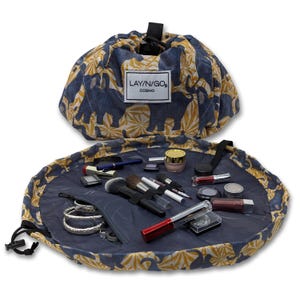 May include: A blue and yellow patterned makeup bag with a drawstring closure. The bag is open and laid flat, revealing a variety of makeup products and brushes. The bag has the text "LAY'N/GO COSMO" printed on it.