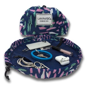 May include: A blue and white patterned lay-n-go travel organizer with a zippered pocket and a drawstring closure. The organizer is open and filled with various items, including a phone, keys, jewelry, and a makeup brush. The organizer is labeled "LAY'N/GO COSMO MINI".