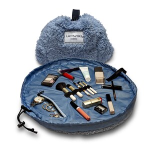 May include: A blue round makeup bag with a drawstring closure. The bag is open and filled with makeup brushes, lipstick, eyeshadow, and other cosmetics. The bag has a fuzzy exterior and a blue lining. The bag has a label that says "Layn/Go Cosmo".