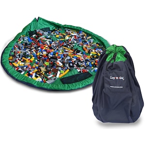 May include: A green and blue round play mat with a drawstring closure. The mat is filled with colorful Lego blocks. A matching drawstring bag with the text "Lay'n Go" and the website "www.layngo.com" is shown next to the mat.