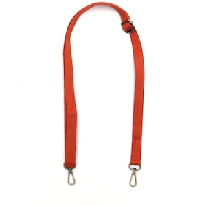 Puede incluir: Correa de lona naranja con dos cierres plateados y una hebilla de latón.