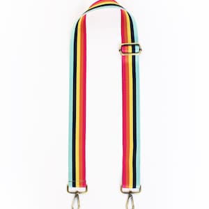 May include: A colorful, striped bag strap with a rainbow design. The strap features a repeating pattern of teal, red, yellow, and black stripes. It has gold-colored metal hardware, including two swivel clasps and a buckle.