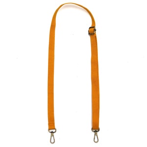 May include: A mustard yellow adjustable strap with two metal clasps. The strap is made of a woven fabric.