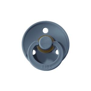 May include: A blue silicone pacifier with a round, flat shape and a textured surface. The pacifier has a small ring for attaching to a clip and the word "BIBS" is printed on the bottom.