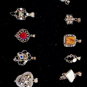May include: A collection of 12 silver pendants with various gemstone and mineral inlays. The pendants are displayed on a black background.