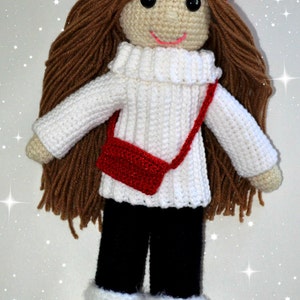 May include: A crocheted doll wearing a red hat, white sweater, black pants, and white boots. The doll has brown hair and a red purse.