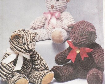 May include: Three handmade teddy bears in various colors. One is beige with a pink bow, another is brown with a red bow, and the third is brown and beige striped with a white bow. The bears have a textured, striped pattern.