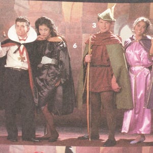 May include: Four people in costume are posing for a photo. A man dressed as a vampire holds a candelabra. A woman wears a black dress and cape. A man is dressed as Robin Hood. A woman wears a pink dress and purple cape.