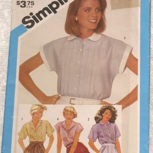 May include: Simplicity sewing pattern featuring a woman wearing a light blue collared shirt with short sleeves. The pattern includes illustrations of similar shirts in different colors. The price is $3.75.