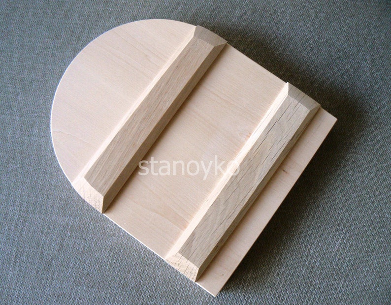 May include: A wooden dough scraper with a rounded top and two wooden strips on the surface. The scraper is made of light wood and has a natural finish.