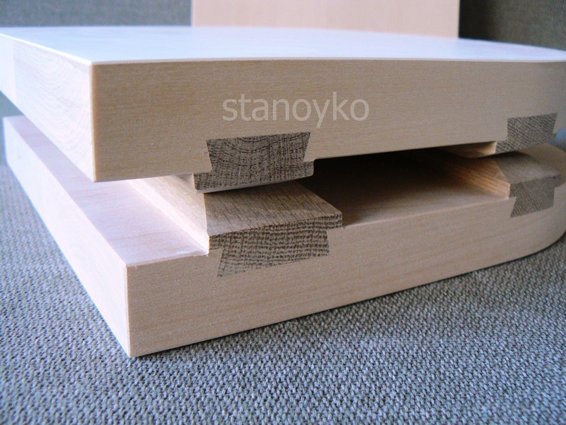 May include: Two pieces of light wood joined together with a dovetail joint. The wood is smooth and has a natural grain. The text "stanoyko" is visible on the top piece of wood.