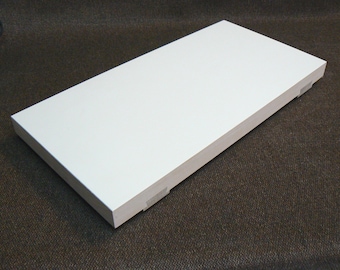 May include: A white rectangular shelf with rounded edges. The shelf is made of wood and has a smooth, matte finish. The shelf is sitting on a brown carpet.