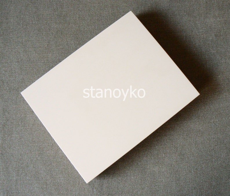 May include: A blank white card on a gray textured surface. The card is rectangular and has a smooth, matte finish.