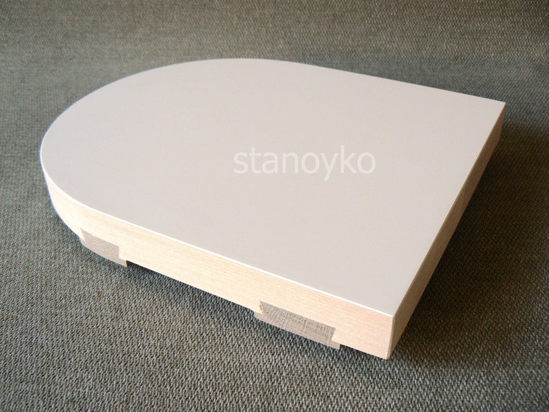 May include: White, rounded, wooden shelf with a smooth, flat surface. The shelf has a slightly curved edge and is supported by a wooden base.