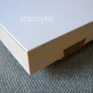 May include: Close-up of the edge of a white wooden frame with a smooth, white surface. The frame is made of natural wood with a light brown color. The text "stanoyko" is visible on the white surface.