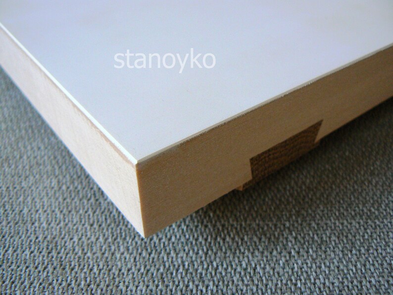 May include: Close-up of the edge of a white wooden frame with a smooth, white surface. The frame is made of natural wood with a light brown color. The text "stanoyko" is visible on the white surface.