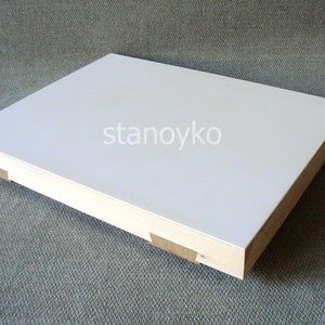 May include: A white rectangular wooden board with a smooth surface. The board has a light wood frame and is sitting on a textured gray surface.