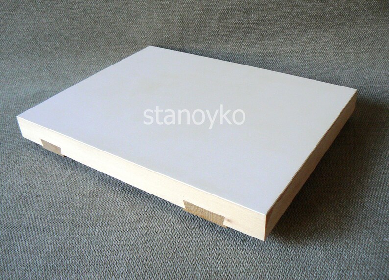 May include: A white rectangular wooden board with a smooth surface. The board has a light wood frame and is sitting on a textured gray surface.