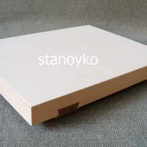 May include: A white rectangular wooden box with a smooth surface and rounded edges. The box is made of light wood and has a white top. The box is sitting on a gray textured surface. The text "stanoyko" is printed on the top of the box.