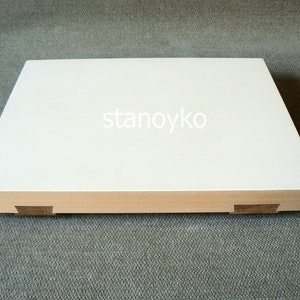 May include: A white rectangular wooden cutting board with rounded edges and a beveled edge. The board has four small wooden feet on the bottom.