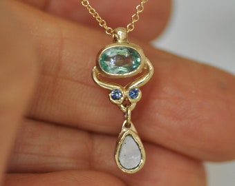 May include: A gold necklace with a pendant featuring a light blue oval gemstone, two smaller blue gemstones, and a teardrop-shaped white gemstone.