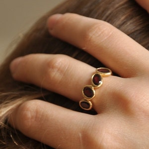 Puede incluir: Un anillo de oro con cinco piedras preciosas rojas ovaladas engastadas en una banda.
