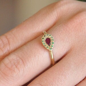 May include: A gold ring with a teardrop-shaped red gemstone surrounded by smaller green gemstones.